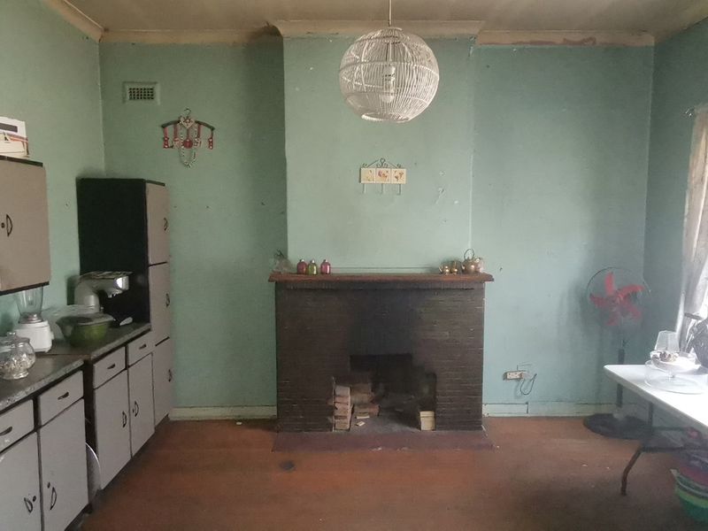 A dated living room featuring a prominent brick fireplace, built-in cabinetry, and original flooring, offering significant potential for renovation and modernization.