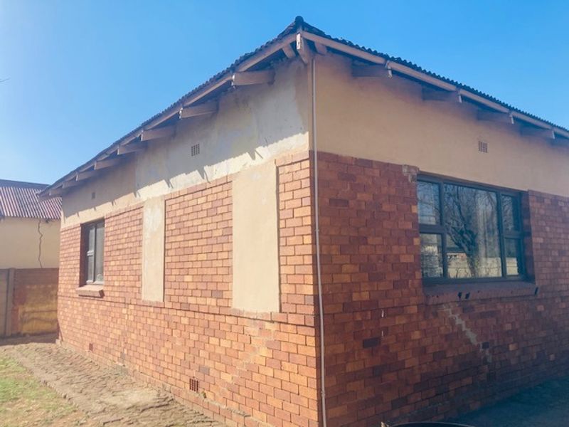 Exterior view of the house showing face brick and plastered walls with visible structural cracking and weathered roof eaves.