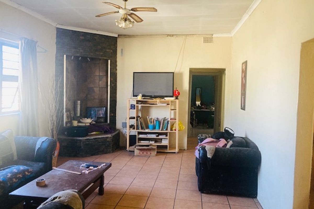 A living room featuring tiled flooring, a corner fireplace, and a ceiling fan, requiring cosmetic updates to improve the overall aesthetic.