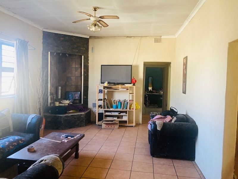 A living room featuring tiled flooring, a corner fireplace, and a ceiling fan, requiring cosmetic updates to improve the overall aesthetic.