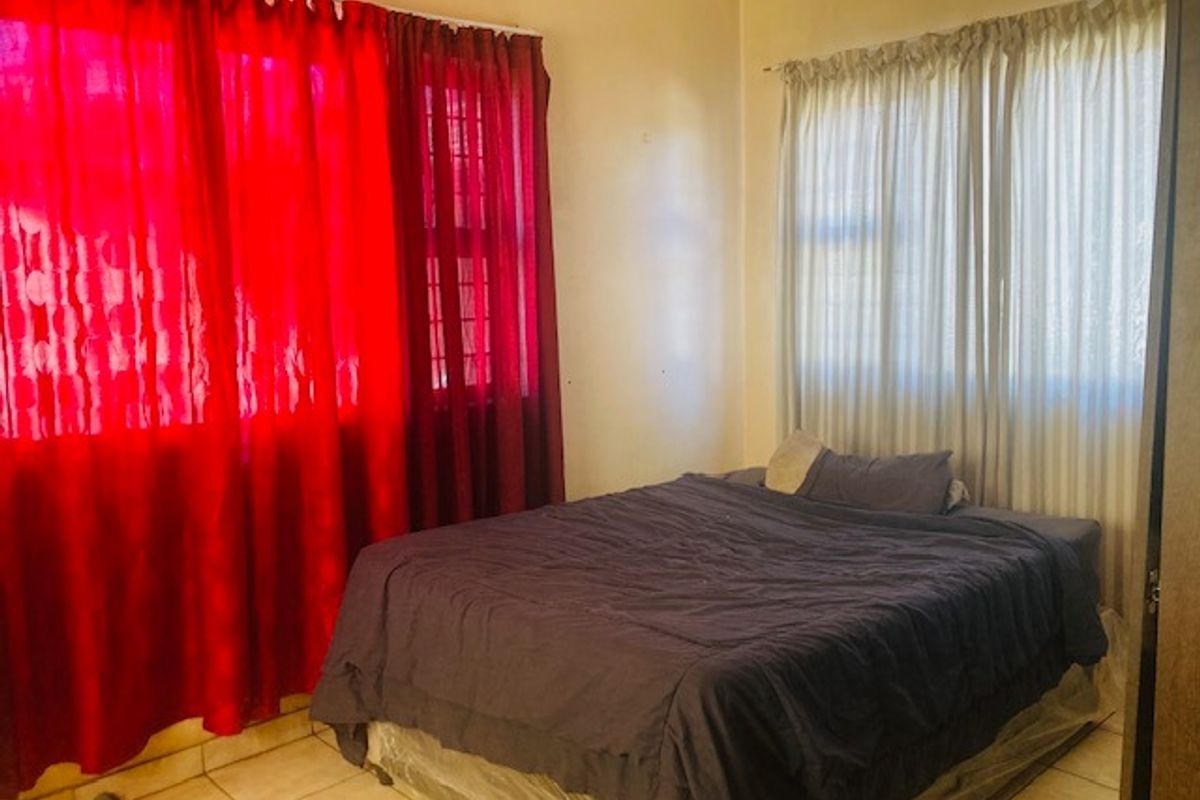 A bedroom featuring tiled flooring and windows fitted with security bars, offering a functional space with natural light.