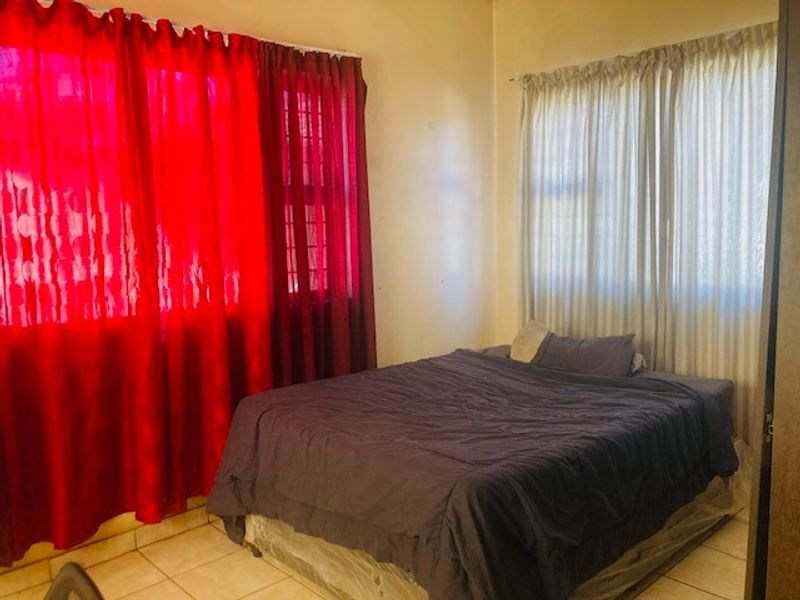 A bedroom featuring tiled flooring and windows fitted with security bars, offering a functional space with natural light.