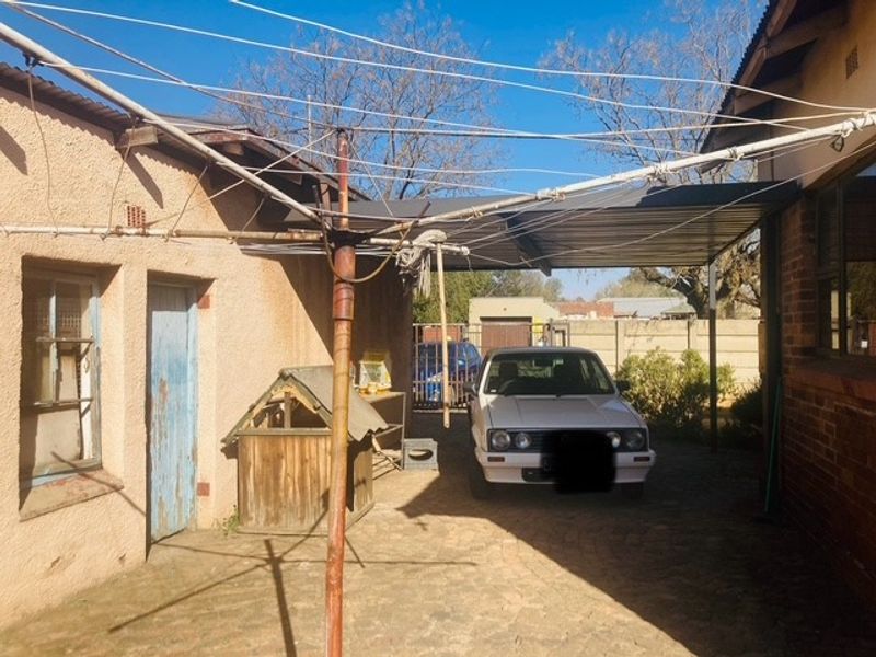Rear exterior area featuring a paved driveway, a covered carport structure, and a rotary clothesline set against the property's rear facade.