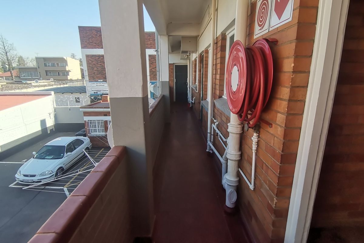 An exterior apartment building walkway featuring brick walls, a fire hose reel, and concrete flooring overlooking the parking area.