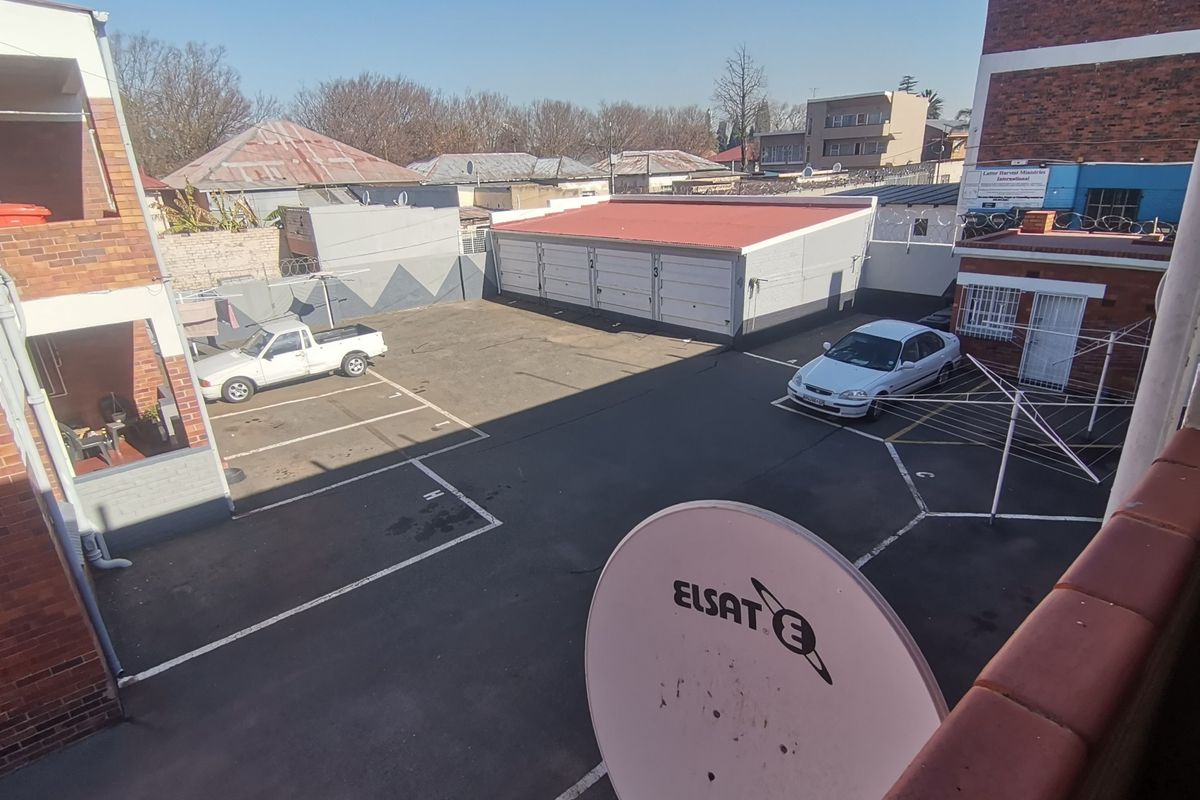 An elevated view of the apartment complex rear parking area featuring a garage block, paved parking bays, and perimeter security fencing.