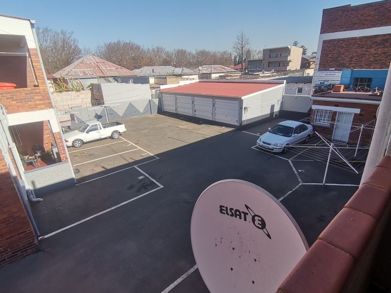 An elevated view of the apartment complex rear parking area featuring a garage block, paved parking bays, and perimeter security fencing.