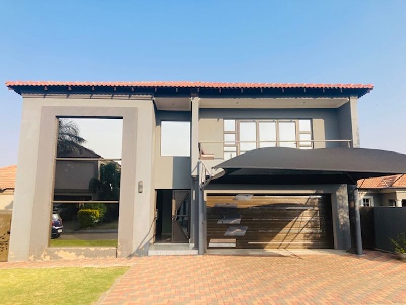 Front elevation of a modern two-story house featuring a double garage, paved driveway, and a balcony with a shade sail.