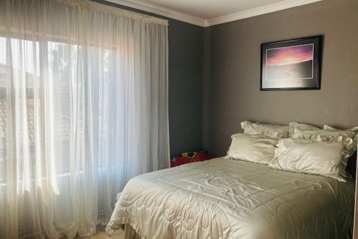 A cozy bedroom featuring crown molding and laminate flooring, with natural light filtering through sheer curtains.