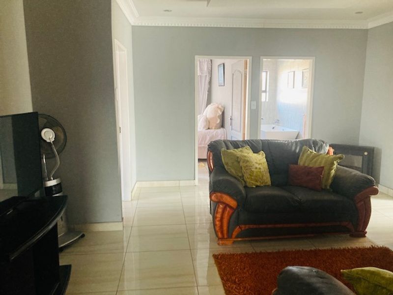 A living room featuring tiled flooring and decorative ceiling molding, with direct access to an adjacent bedroom and bathroom area.