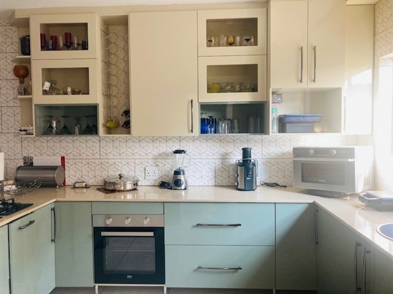 A well-maintained kitchen featuring light-toned cabinetry, stone countertops, a geometric tile backsplash, and built-in oven and hob.