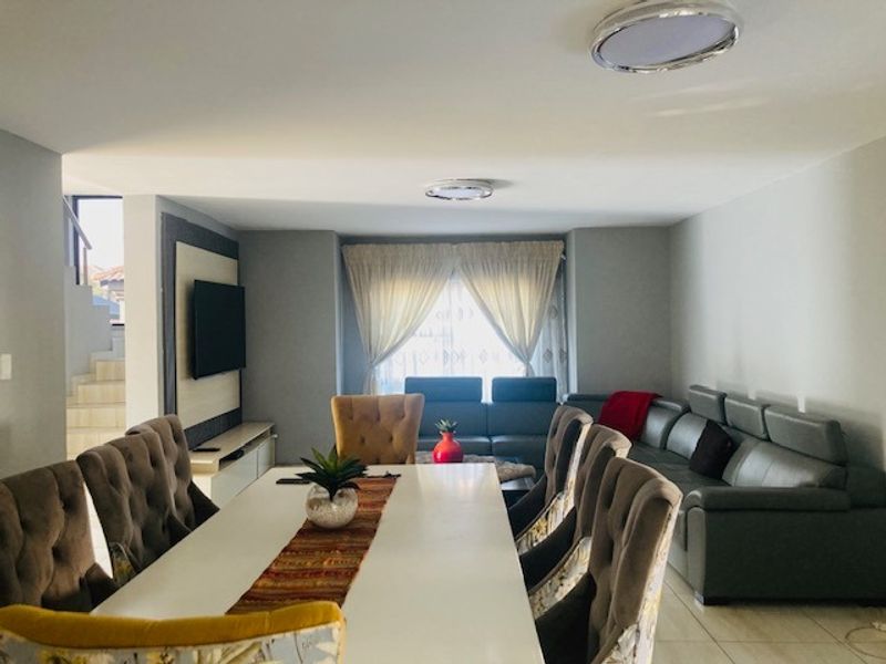 Spacious open-plan living and dining area featuring neutral tiled flooring, modern recessed ceiling lighting, and a dedicated built-in media wall.