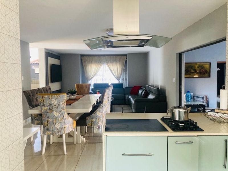 An open-plan living and dining area featuring a modern kitchen island with a built-in hob and extractor fan, flowing into a spacious lounge.