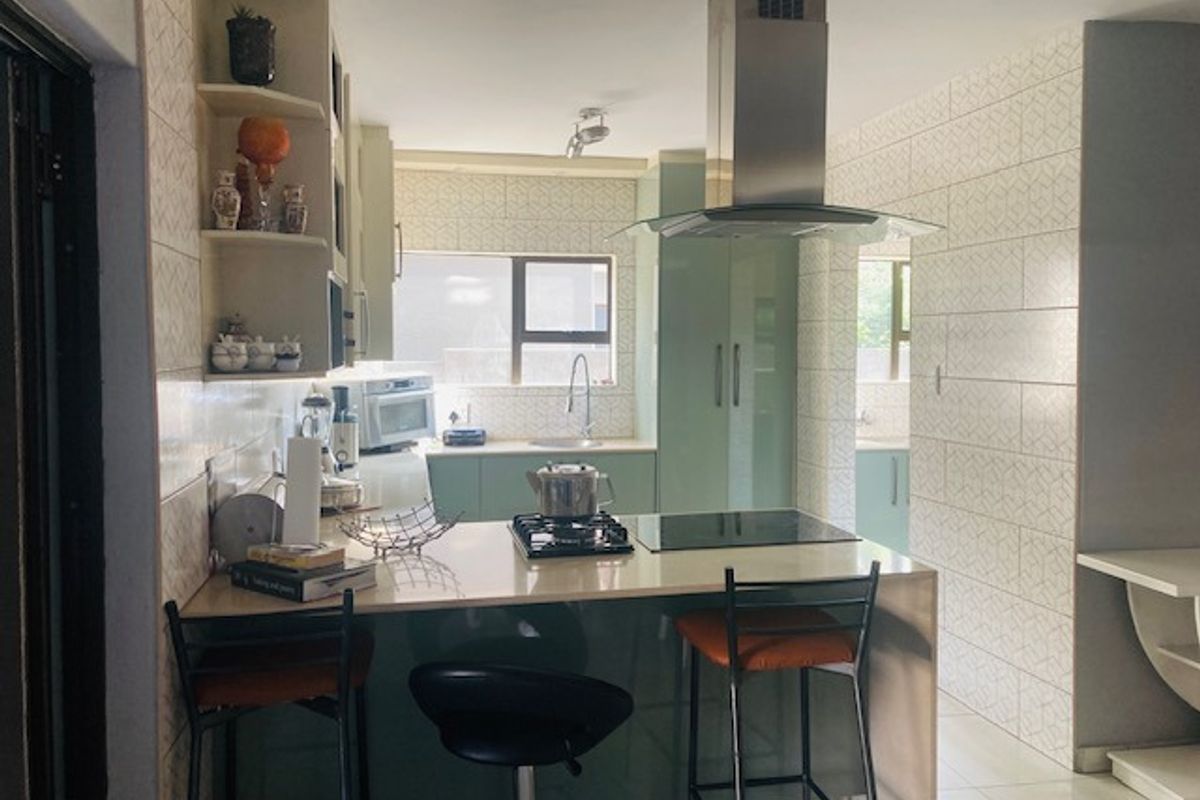 Modern kitchen featuring a central island with a gas hob and electric cooktop, stainless steel extractor fan, stone countertops, and ample built-in cabinetry.