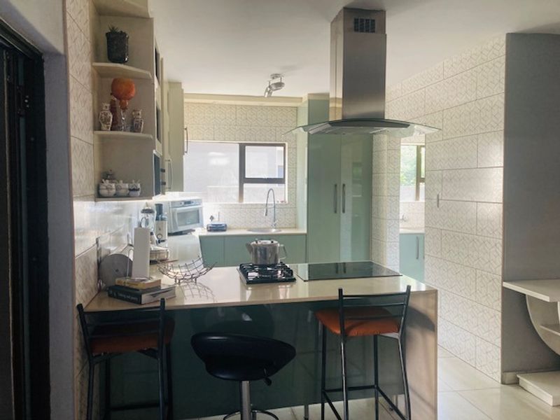 Modern kitchen featuring a central island with a gas hob and electric cooktop, stainless steel extractor fan, stone countertops, and ample built-in cabinetry.