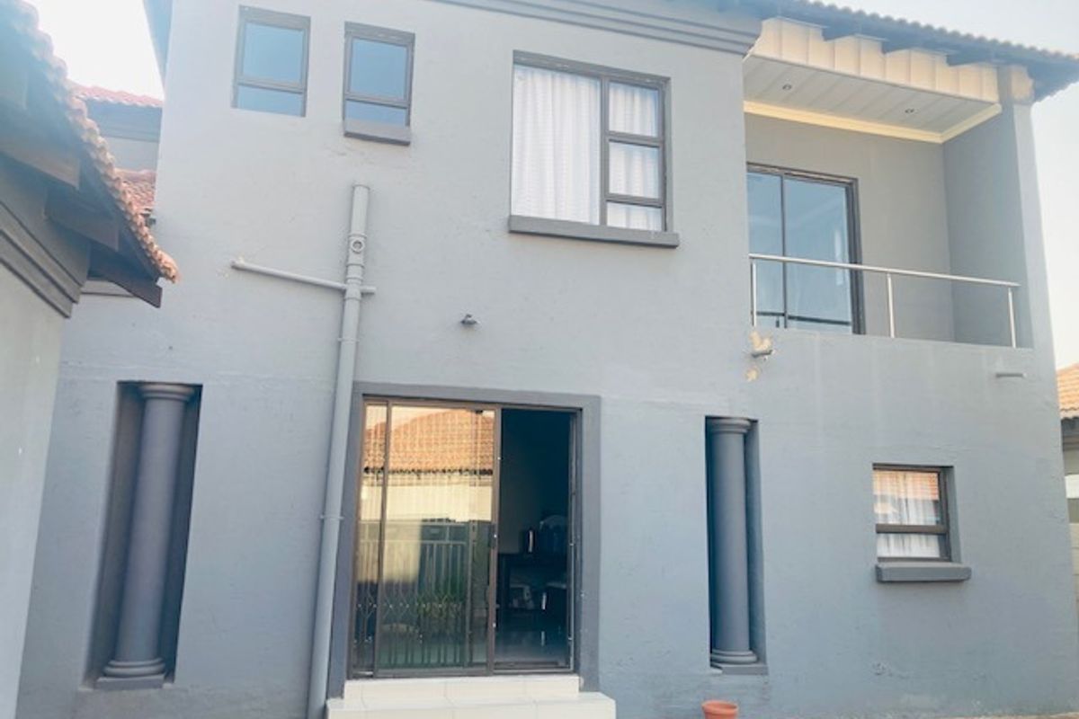Rear elevation of a two-story house featuring a balcony with stainless steel balustrade, sliding glass doors, and decorative columns on a paved patio area.