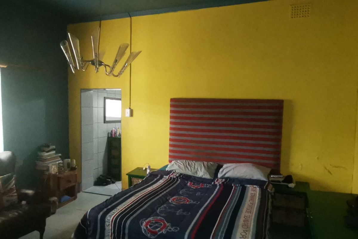 A bedroom featuring bold yellow and dark teal wall finishes, a central light fixture, and an adjoining doorway leading to a tiled space.