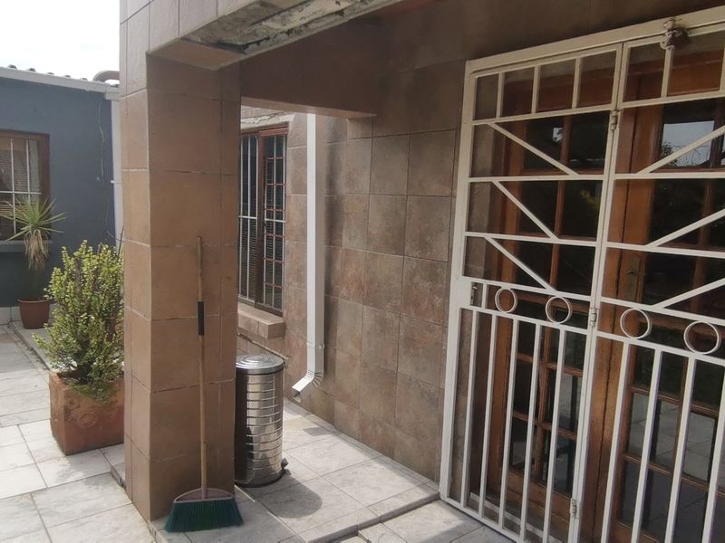 A covered patio area featuring tiled flooring, wall cladding, and a secure metal gate leading to the interior.