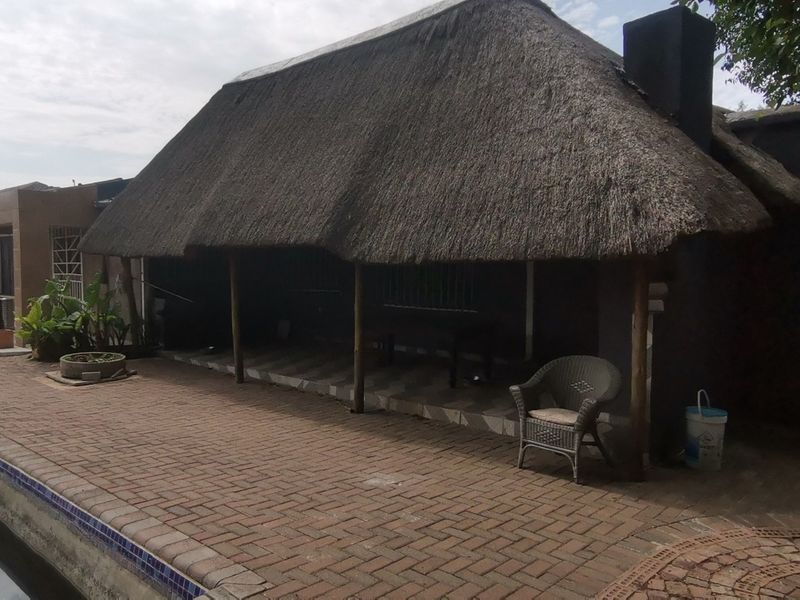 Outdoor entertainment area featuring a thatched roof patio, brick paving, and an adjacent swimming pool, offering potential for exterior renovation.