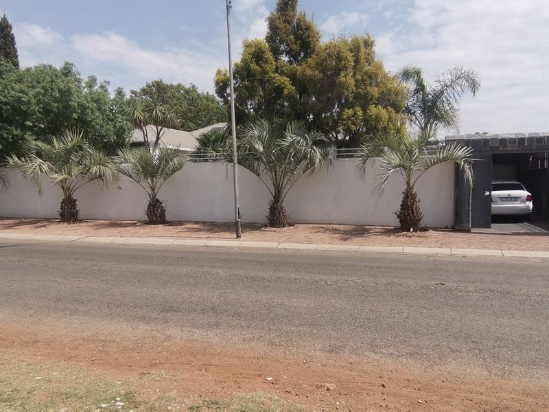 Street view of the property featuring a long perimeter wall, landscaped palm trees, and a covered carport area.