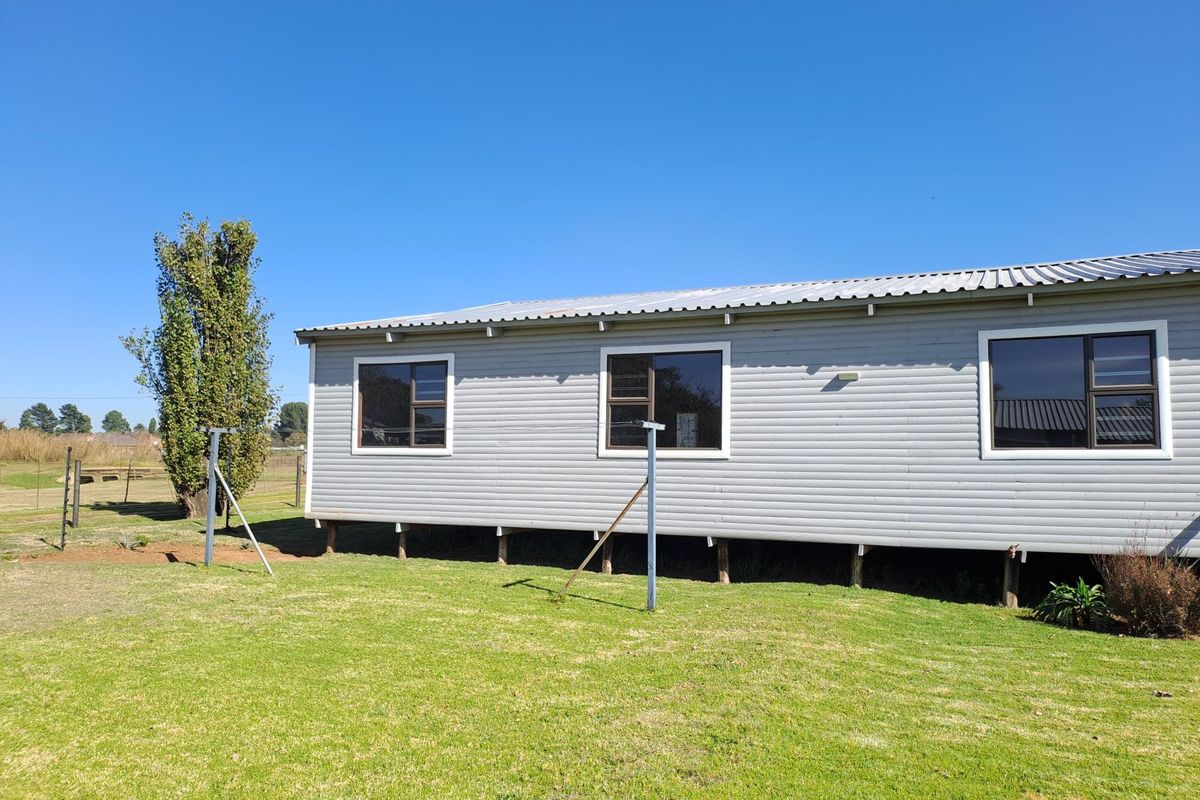 A rear view of a single-story house featuring horizontal cladding, aluminium windows, and a corrugated metal roof, set on raised foundation posts.