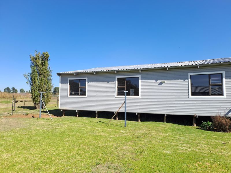 A rear view of a single-story house featuring horizontal cladding, aluminium windows, and a corrugated metal roof, set on raised foundation posts.
