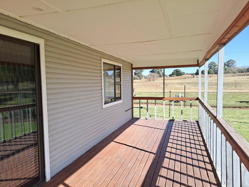 A covered timber deck patio featuring weatherboard cladding and a balustrade, offering an open view of the surrounding rural landscape.