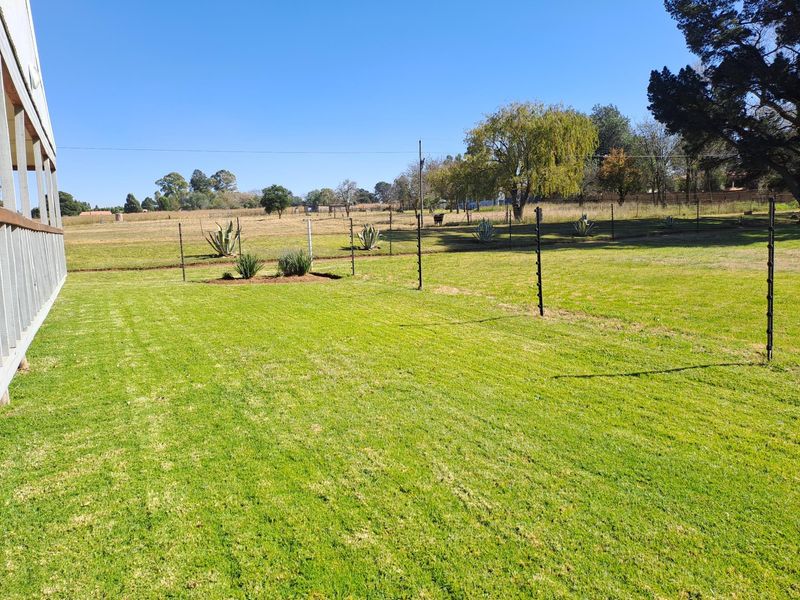 A spacious, well-maintained lawn area featuring an electric fence boundary and an adjacent timber deck, offering open views of the surrounding landscape.