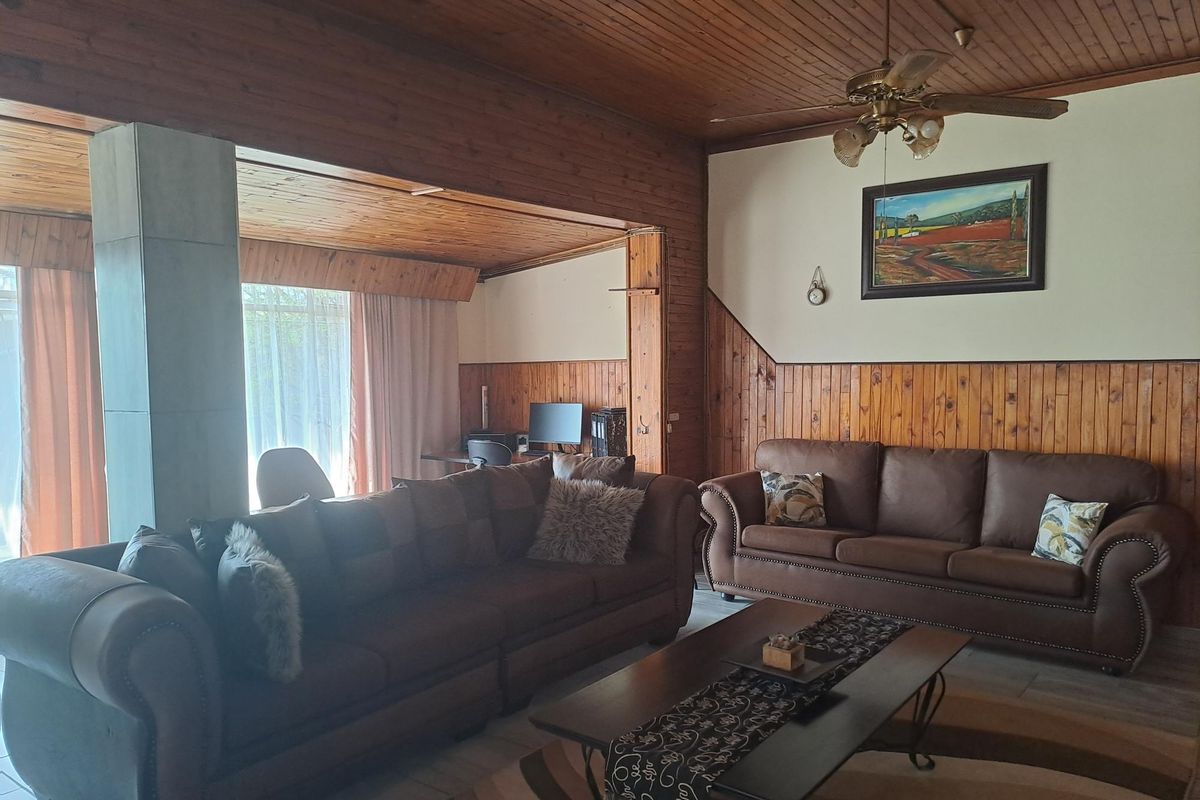 Spacious living room featuring extensive timber ceiling and wall paneling, tiled flooring, and a central ceiling fan.