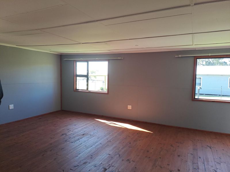 An empty bedroom featuring timber flooring, grey painted walls, and aluminium-framed windows with a drop ceiling.
