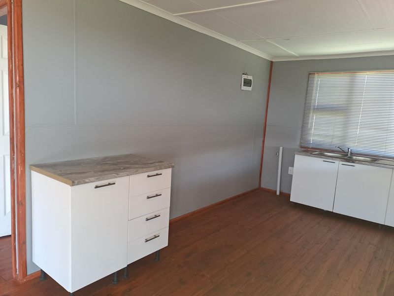 A basic kitchen area featuring white cabinetry, laminate countertops, a stainless steel sink, and wood-look flooring in a simple, functional layout.