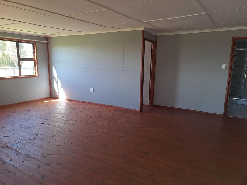 An empty bedroom featuring timber flooring, grey panelled walls, and an en-suite bathroom access point.
