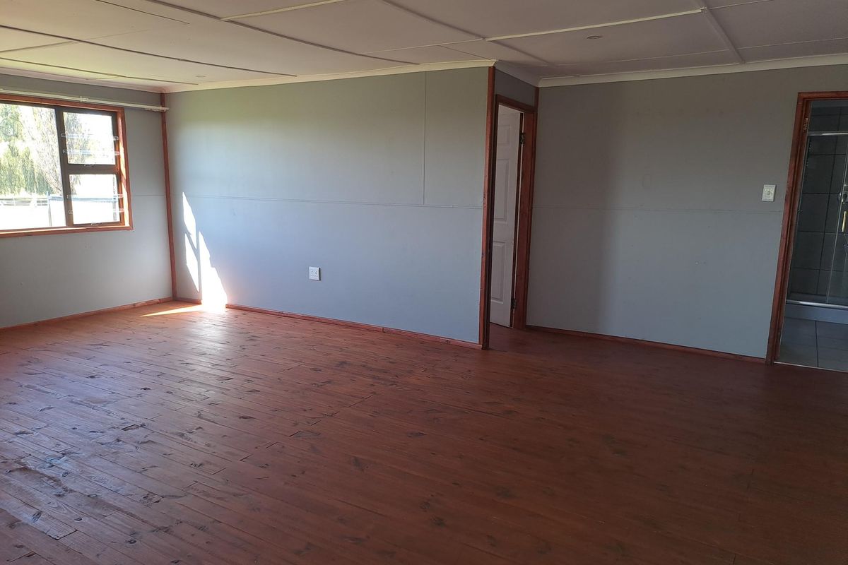 An empty bedroom featuring timber flooring, grey panelled walls, and an en-suite bathroom access point.