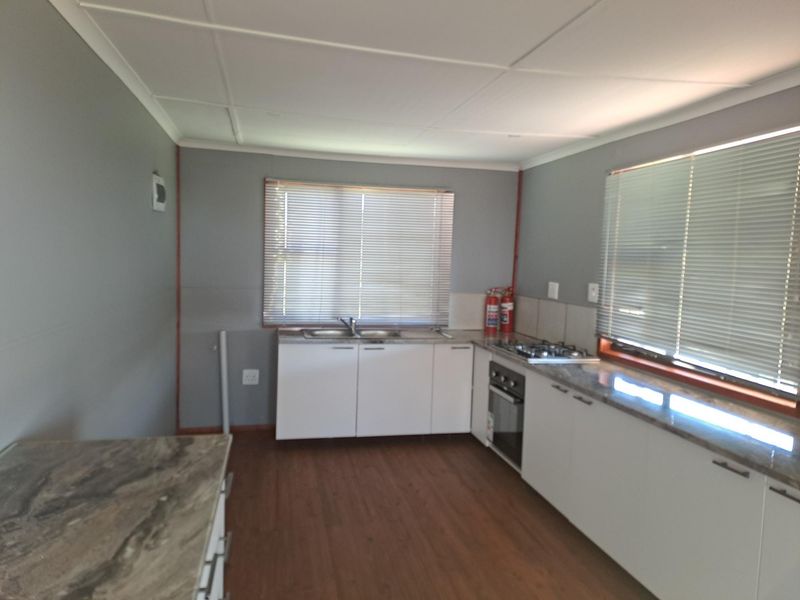 A functional kitchen featuring white cabinetry, a built-in oven, gas hob, stainless steel sink, and laminate flooring with neutral grey walls.