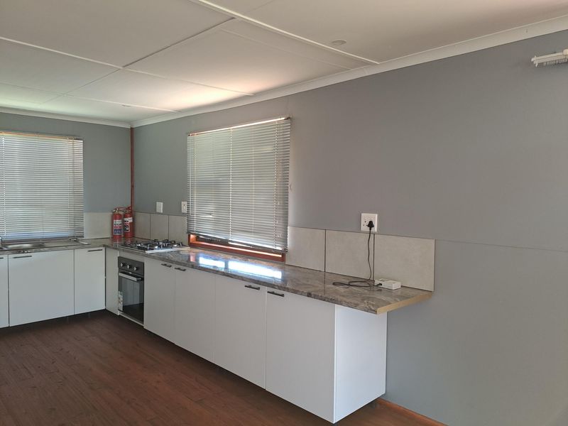 A clean, modern kitchen featuring white cabinetry, stone-look laminate countertops, a built-in oven, gas hob, and neutral grey walls.
