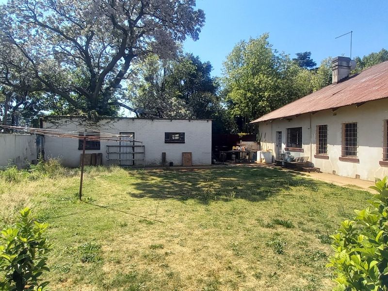 Rear view of the property featuring a large garden, an outbuilding, and a main house structure with a corrugated metal roof and security bars.