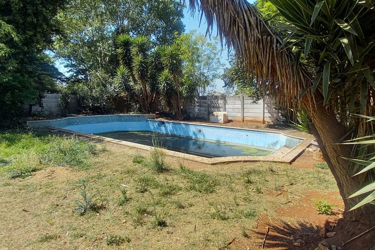 Outdoor pool area featuring a swimming pool and perimeter boundary wall, currently requiring significant maintenance and landscaping attention.