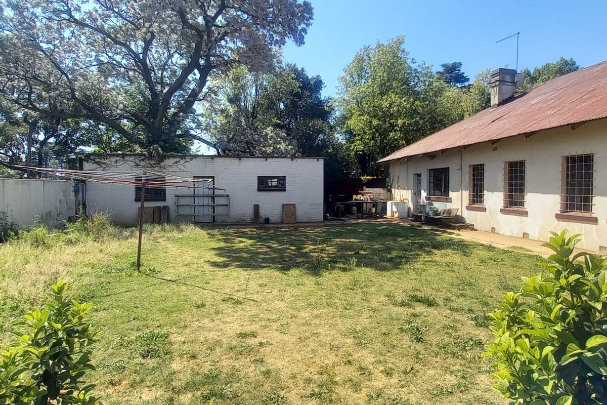 Rear view of the property featuring a large garden, corrugated metal roof, and security bars on the windows.