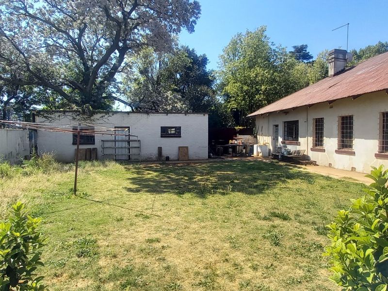Rear view of the property featuring a large garden, corrugated metal roof, and security bars on the windows.