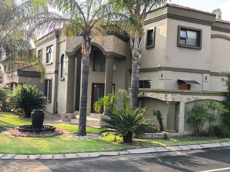 A double-story residential property featuring stone cladding, an arched entrance with columns, a tiled roof, and a landscaped front garden with a water feature.