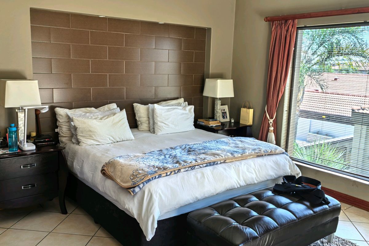 A bedroom featuring a tiled floor, a large window with natural light, and a prominent brown tiled feature wall behind the bed area.