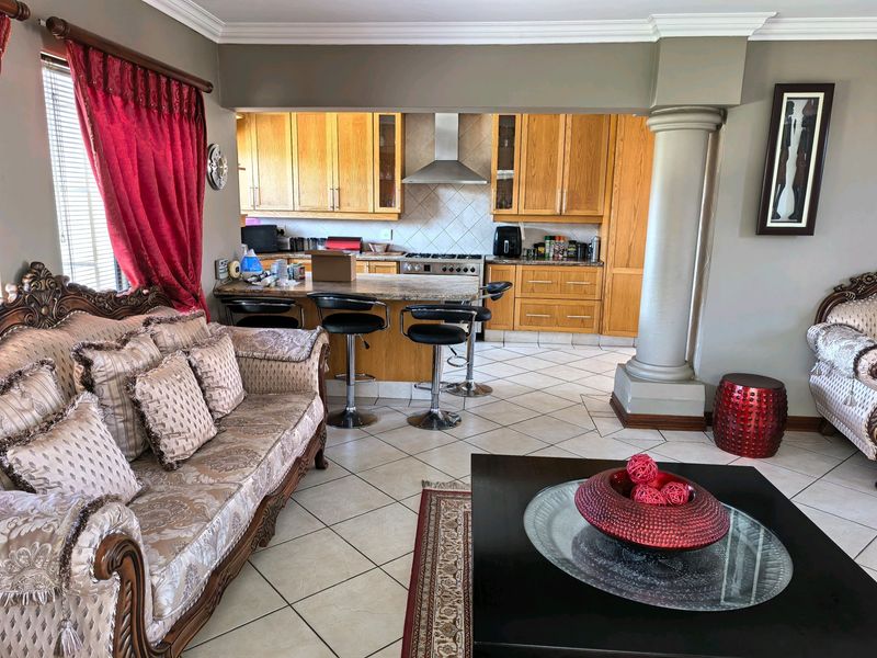 Open-plan living and kitchen area featuring wooden cabinetry, granite countertops, a gas hob, tiled flooring, and a decorative structural column.