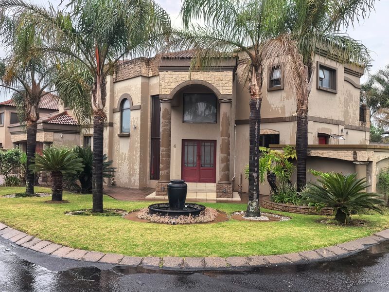 Front elevation of a multi-story residence featuring stone cladding, arched entryway with columns, and a landscaped front garden with a central water feature.