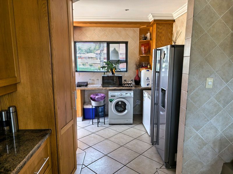 A functional scullery area featuring wooden cabinetry, granite countertops, tiled splashbacks, and dedicated space for laundry appliances.