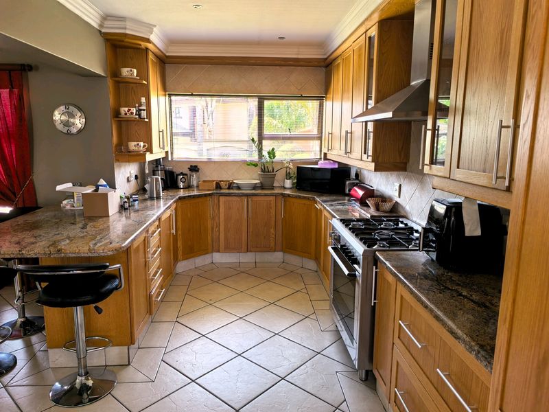 A functional kitchen featuring wooden cabinetry, granite countertops, a gas stove with extractor fan, and tiled flooring with a breakfast bar area.