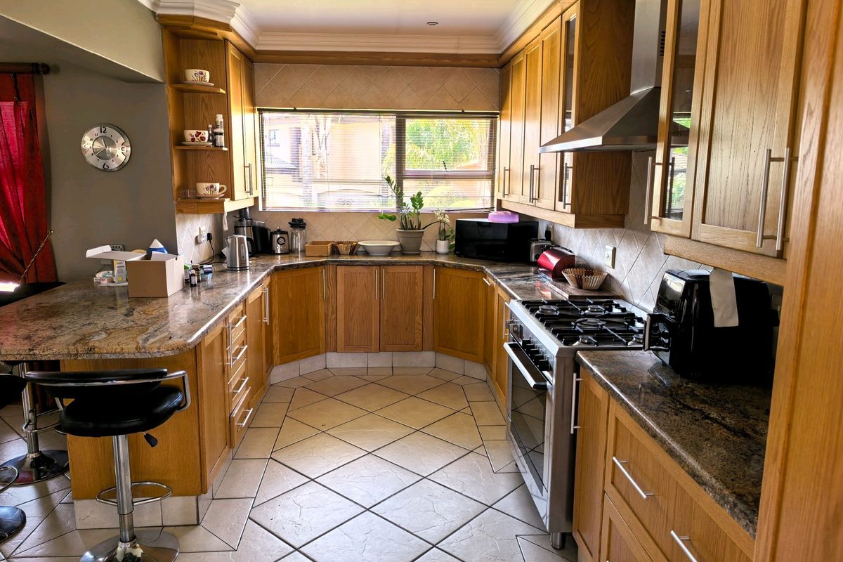 A functional kitchen featuring wooden cabinetry, granite countertops, a gas stove with extractor fan, and tiled flooring with a breakfast bar area.
