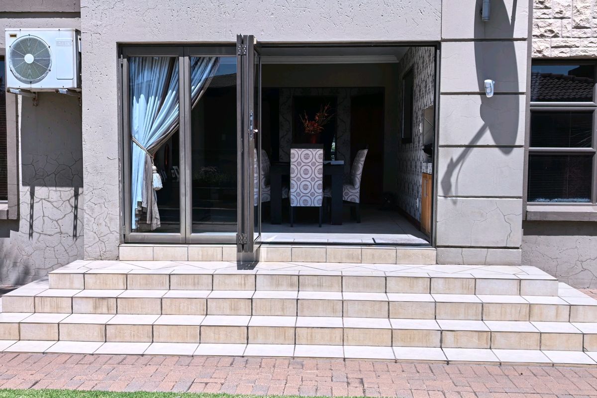 Rear exterior view featuring tiled patio steps leading to an open-plan living area through aluminium stacker doors, with visible exterior wall cracking.