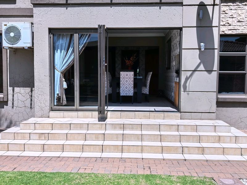 Rear exterior view featuring tiled patio steps leading to an open-plan living area through aluminium stacker doors, with visible exterior wall cracking.