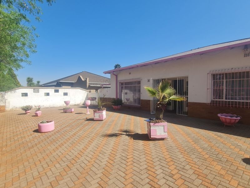 Front exterior view of the house featuring a large paved courtyard area, security bars on windows, and a perimeter boundary wall.