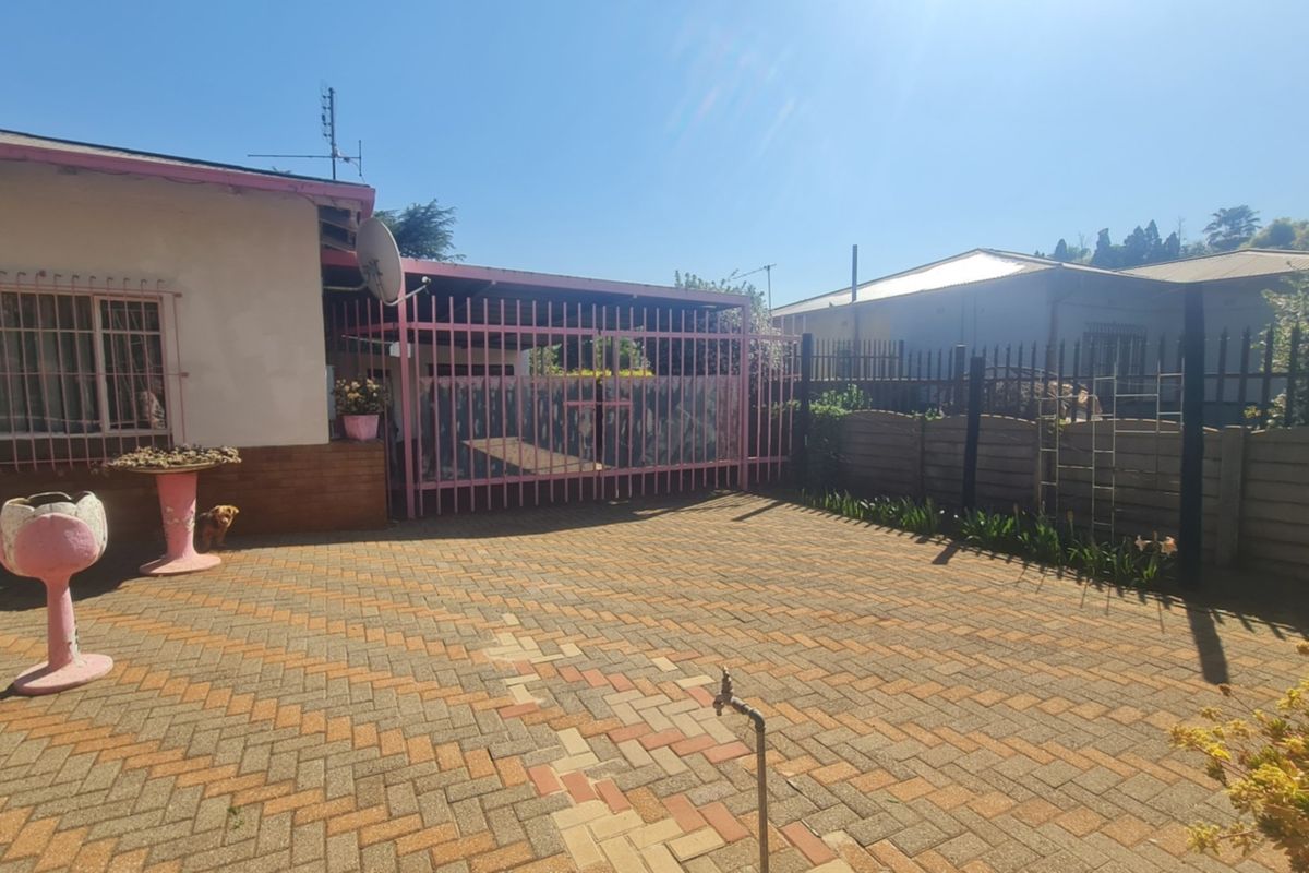 Front exterior view featuring a paved driveway, secure metal gate, and perimeter fencing with security bars on the windows.