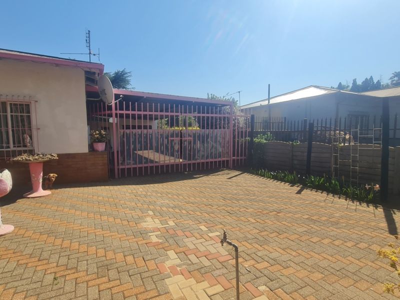 Front exterior view featuring a paved driveway, secure metal gate, and perimeter fencing with security bars on the windows.